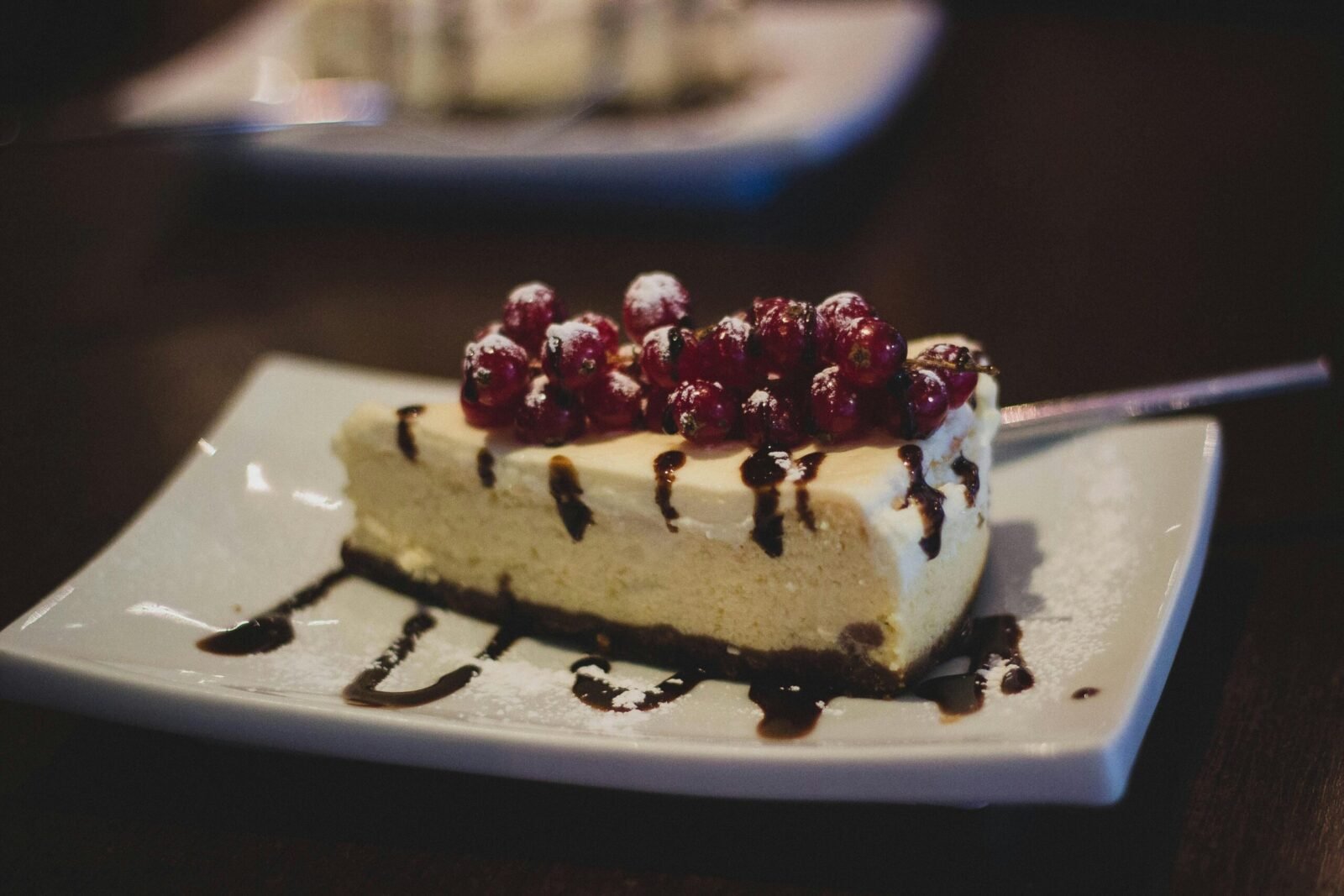 Slice of cheesecake topped with berries and chocolate drizzle on a plate.
