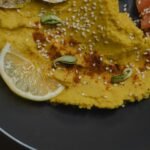 Close-up of creamy hummus with lemon slices and sesame seeds on a black plate.
