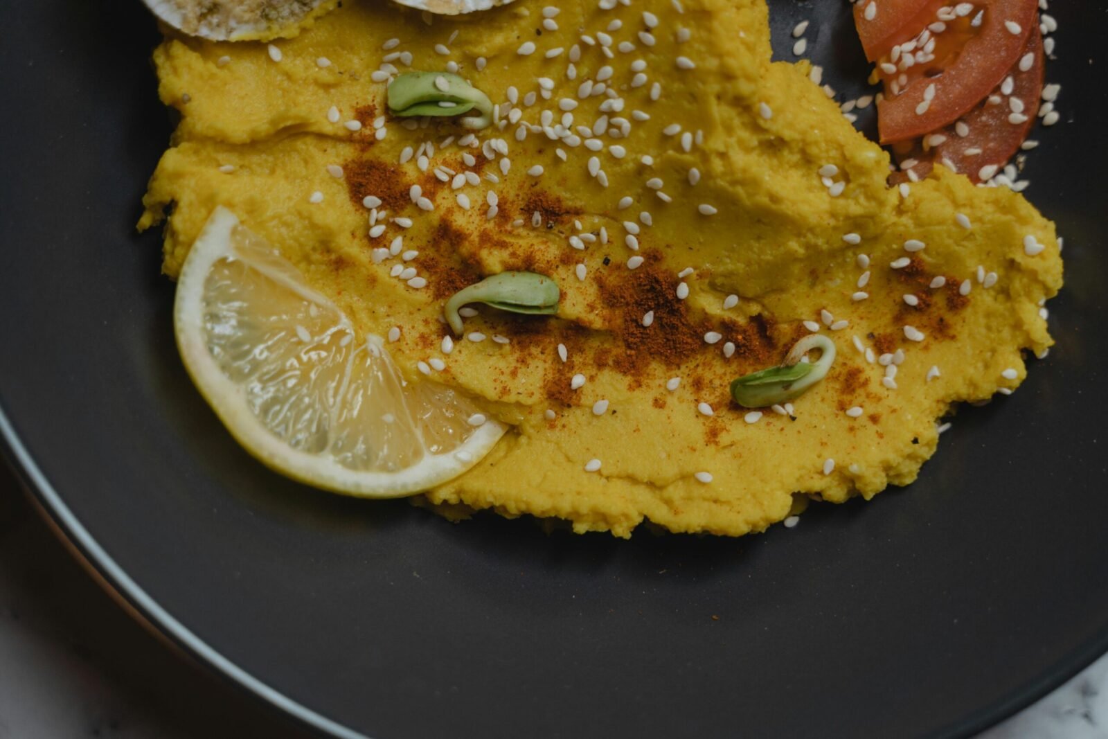 Close-up of creamy hummus with lemon slices and sesame seeds on a black plate.